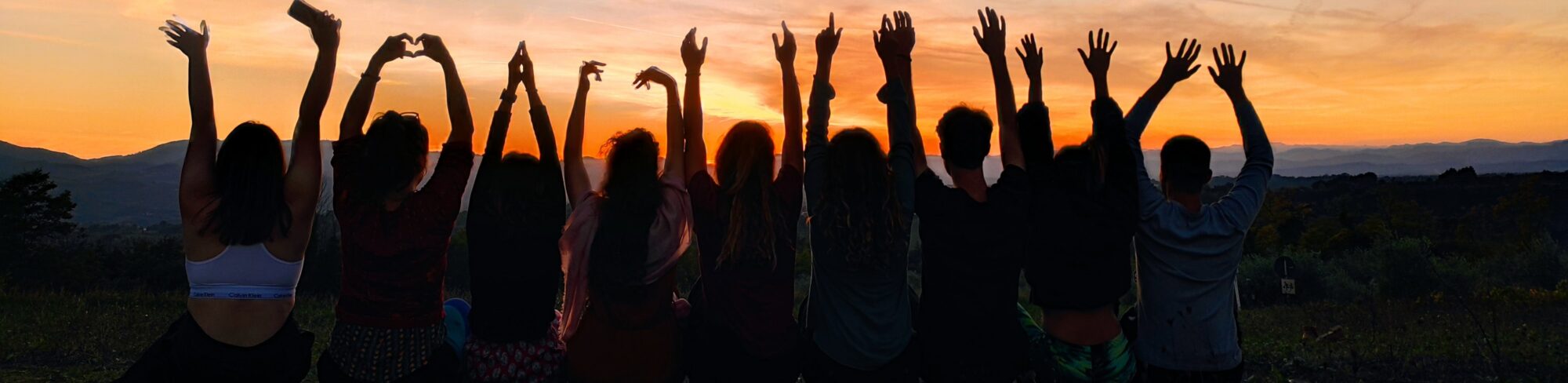 Girls on a bench watching sunset with arms up